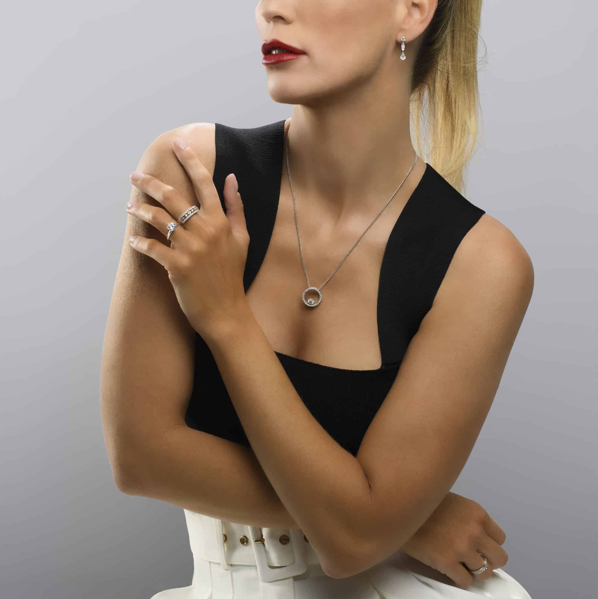Model wearing a combination of diamond wedding, engagement ring, diamond circle pedant and diamond earrings